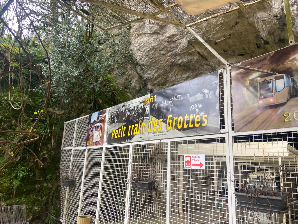 Entrance to the Petit Train des Grottes featuring a sign with its name and historical photos on display.